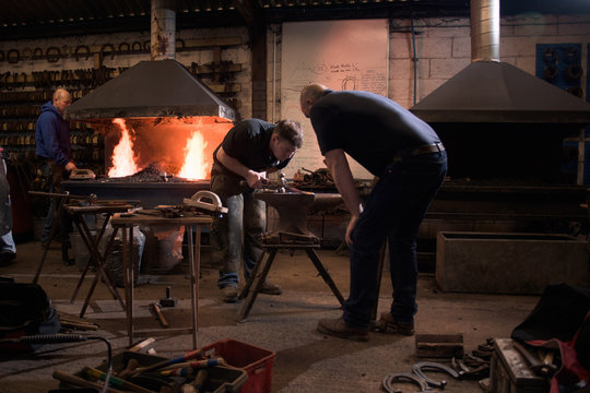 Farriers forging horseshoe on anvil