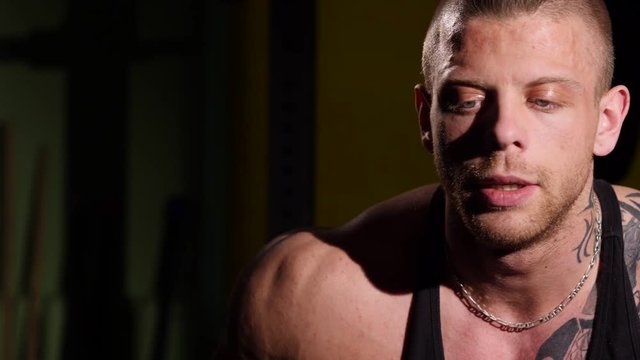 Intense sweaty dramatic portrait of young muscular tired man resting after a training. 60 to 24fps 4K UHD
