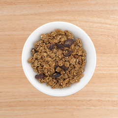 Organic cranberry nut granola in a small white bowl atop a wood table top.