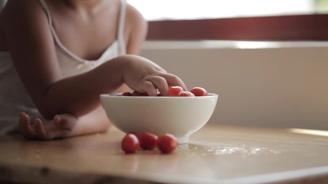 Little girl sits by the table and eating cherry tomato