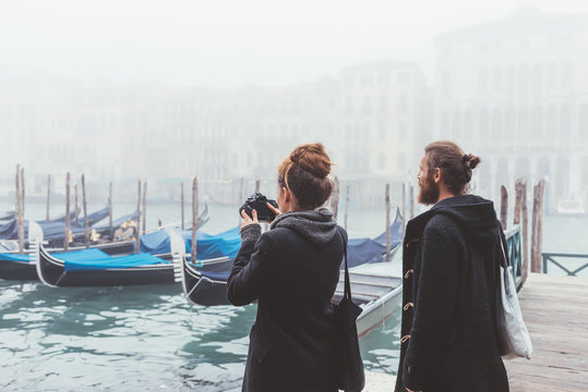 Couple photographing gondolas on misty canal, Venice, Italy