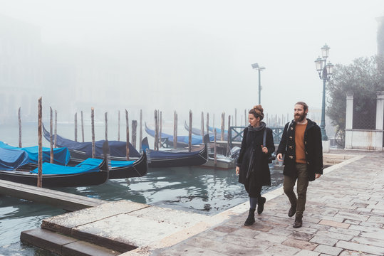 Couple strolling along misty canal waterfront, Venice, Italy