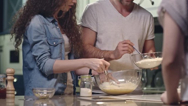 Tracking shot of woman whisking batter in glass bowl and man adding flour on kitchen counter