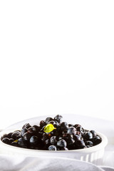 Pile blueberries in white ceramic bowl stay on white organic material.
