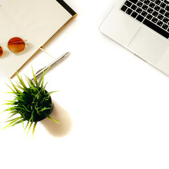 Modern home workspace with bright sunglasses, laptop keyboard, green office plant and notebook. White background, top view, flat lay