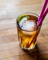 Long island iced tea cocktail with lime, ice and served with pink straw.