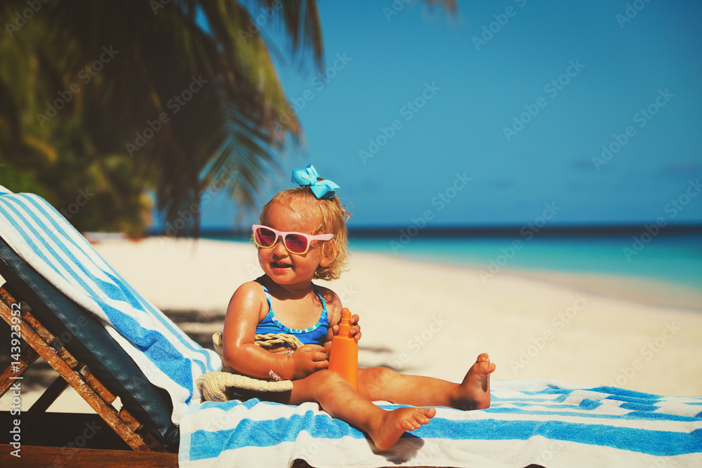 Wall mural cute little girl with sunblock cream on beach