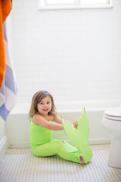Portrait of girl in lime green mermaid costume sitting on bathroom floor