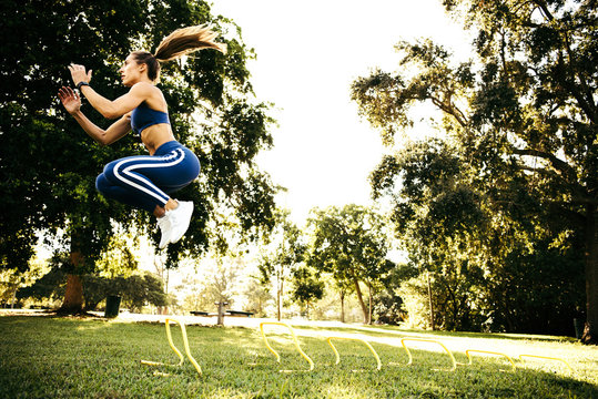 Young woman training, jumping between agility hurdles in park