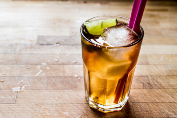 Long island iced tea cocktail with lime, ice and served with pink straw.
