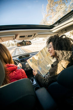 Woman driving car, friend in passenger seat looking at map