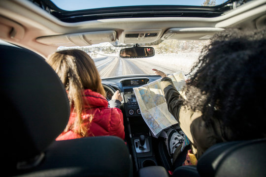 Woman driving car, friend in passenger seat looking at map