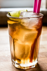 Long island iced tea cocktail with lime, ice and served with pink straw.