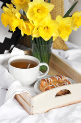 Wooden tray with light breakfast and flowers on white textile in bed. Herbal tea Breakfast in bed Morning Yellow daffodils.