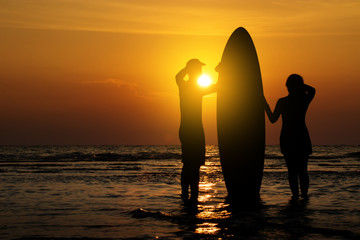 Man and girl with surfboard on the beach at sunset
