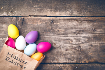 Easter bunny in a paper bag on old boards. Rabbit. Old board background. Easter ideas. Easter eggs. Space for text. Image in trendy toning. On the package text Happy Easter