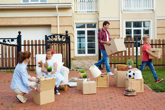 Little girl talking to her mother while packing boxes, man and boy carrying out packed things