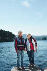 Fototapeta premium Active pensioners with backpacks looking at camera with lake on background