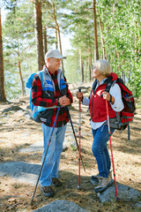 Active couple of retired people with backpacks talking in the forest while trekking