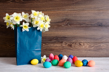 Fototapeta na wymiar Colorful Easter eggs in the basket with lovely bouquet of narcissus and funny bunny on wood background