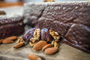 Plums and almonds are next to a chocolate cake on a wooden board.