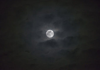 Glowing full moon behind wispy layers of moody clouds, atmospheric night sky scene