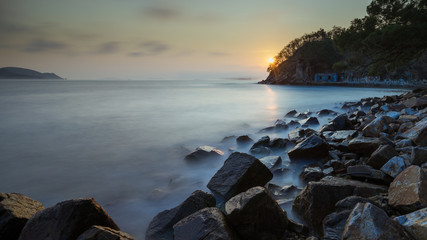 Smooth water sea coast in sunset, islands at background, rocks at foreground