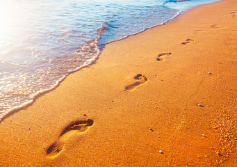 beach, wave and footprints at sunset time