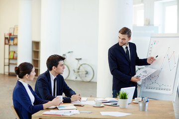 Businessman explaining graph on whiteboard and consulting colleagues
