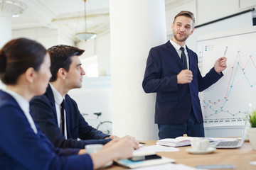 Young confident man pointing at whiteboard while explaining graph
