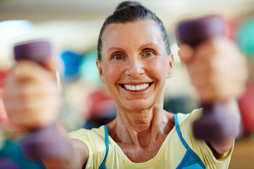 Mature woman with toothy smile exercising with dumbbells