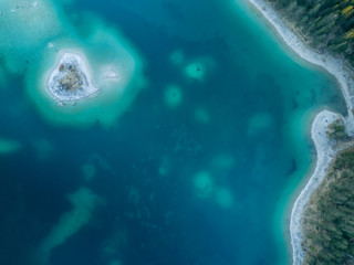 Birds view of a island on the Eibsee. On the island there is a small cabin surrounded by trees.