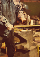 Making of horseshoe. Male worker with hammer making nail holes on horseshoe.