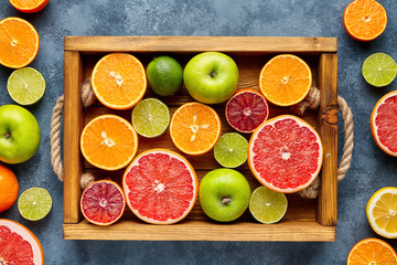 Citrus fruits sliced mix flat lay in wooden tray on blue concrete background, healthy vegetarian organic food, antioxidant detox diet. Tropical summer mix grapefruit, orange, apple, kiwi fruit, lime