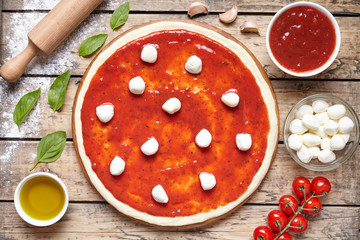Pizza cooking preparation. Baking ingredients on the wooden table: dough, mozzarella, tomatoes sauce, basil, olive oil, tomatoes, cheese, spices. Italian food cuisine background pizza margherita © GreenArt Photography