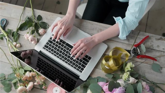 Office workplace essentials: laptop, paper notebook, bouquet of flowers on the rustic wooden table background, florist workplace, Flower business woman.