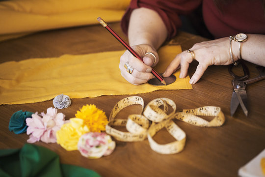 A woman drawing around a small template placed on yellow fabric. 