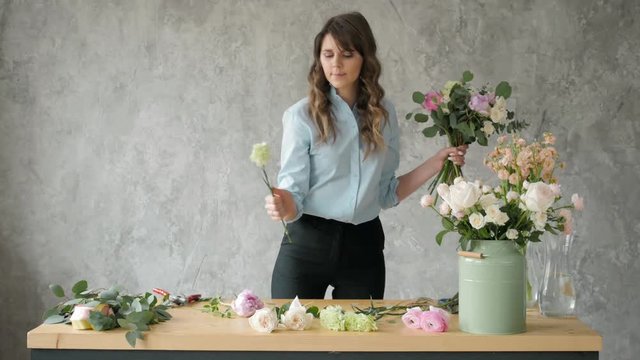 Florist at work: pretty young blond woman holds fashion modern bouquet of different flowers with peone and roses in craft paper