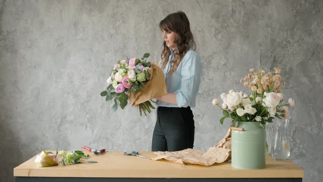 Florist at work: pretty young blond woman holds fashion modern bouquet of different flowers with peone and roses in craft paper