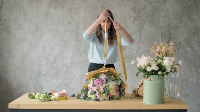 Florist at work: pretty young blond woman holds fashion modern bouquet of different flowers with peone and roses in craft paper