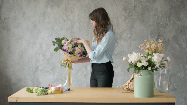Florist at work: pretty young blond woman holds fashion modern bouquet of different flowers with peone and roses in craft paper