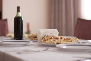 Traditional Bulgarian banitsa, slices, on the ceramic plate and Spanish wine bottle without any label, surrounded by of the focus ceramic plates out and napkin holder. .