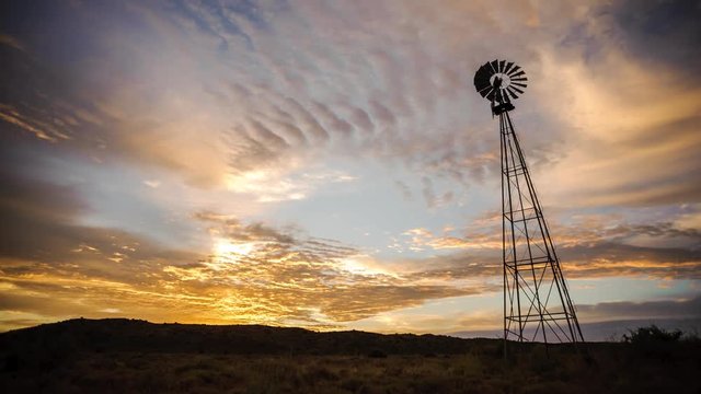 Dramatic linear timelapse sunrise with scattered clouds changing color with a silhouetted windmill in the foreground in a scenic landscape setting with a mountain range in the background available on request.