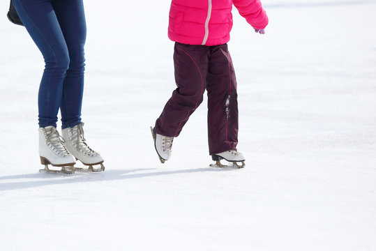 the legs of an adult and child skating on the ice rink.