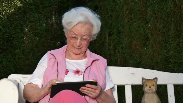 Seniorin mit Tabletcomputer auf Gartenbank