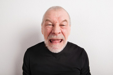 Senior man making funny face, studio shot.