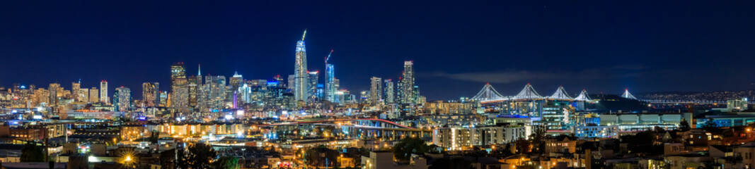 Fototapeta na wymiar San Francisco skyline night panorama with city lights, the Bay Bridge and trail lights