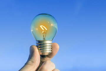 Concept idea of a burning incandescent lamp in a hand against a clear blue sky background from solar energy power