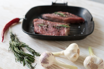 raw steak on cast iron frying pan with garlic and pepper.