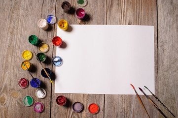 Paper, watercolors, paint brush and some art stuff on wooden table